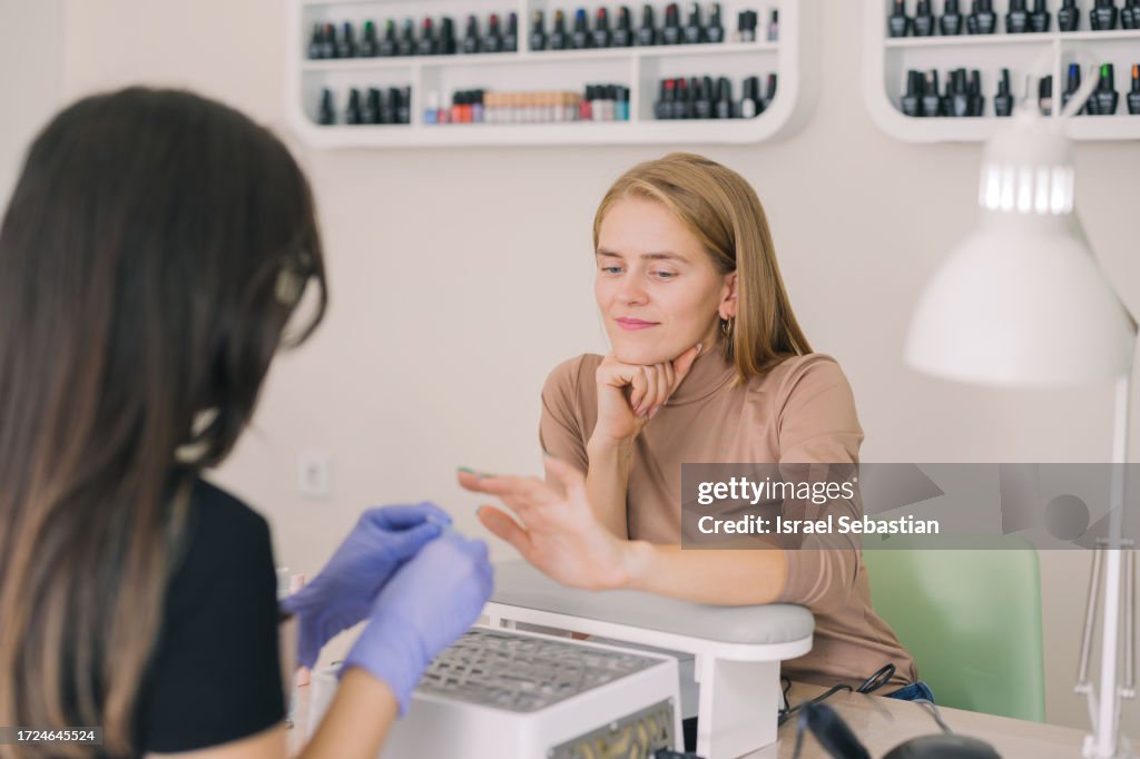 Pretty blonde woman looking at her nails in a happy way for the good job done by her manicurist.