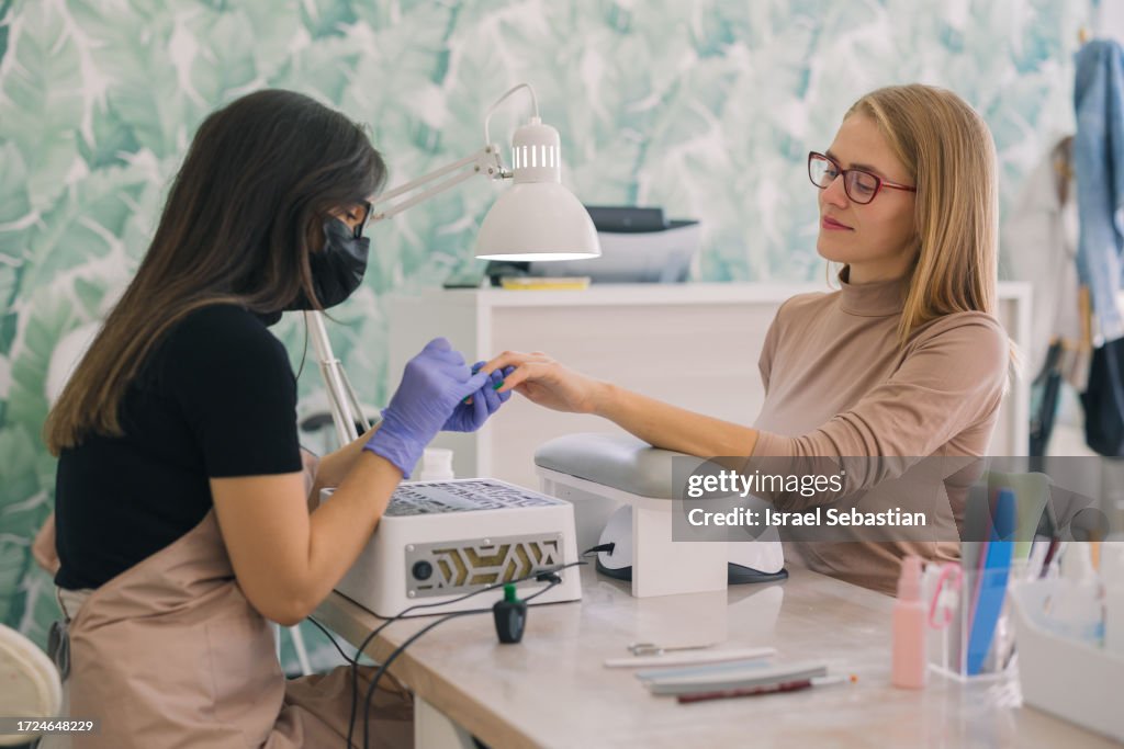 A beautician painting a client's nails in her beauty salon.