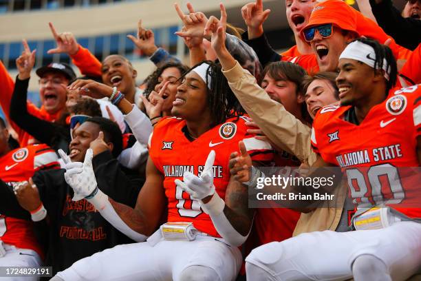 Ollie Gordon II and Brennan Presley of the Oklahoma State Cowboys jump into the stands with fans after defeating the Kansas Jayhawks 39-32 at Boone...