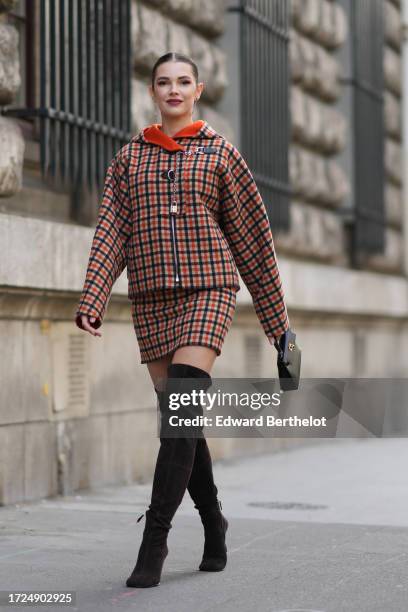 Polina Erofeeva wears a black and orange checkered hoodie jacket, matching short skirt, thigh high black boots, outside Hermes, during the Womenswear...
