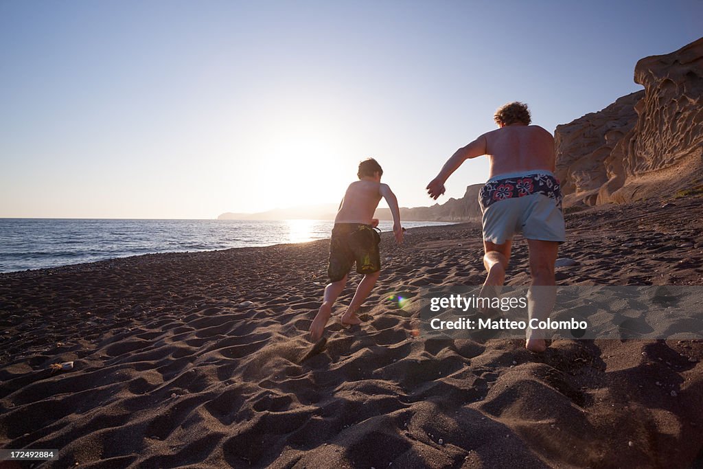 Adult man and child running on a beach at sunset