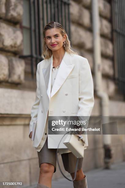 Xenia Adonts wears a white oversized blazer jacket, a Hermes bag, brown leather shorts, suede knee high boots, outside Hermes, during the Womenswear...