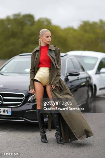 Caroline Daur wears red pullover, a golden bodysuit, a green khaki trench coat, a mini bag, knee high leather boots, outside Loewe, during the...