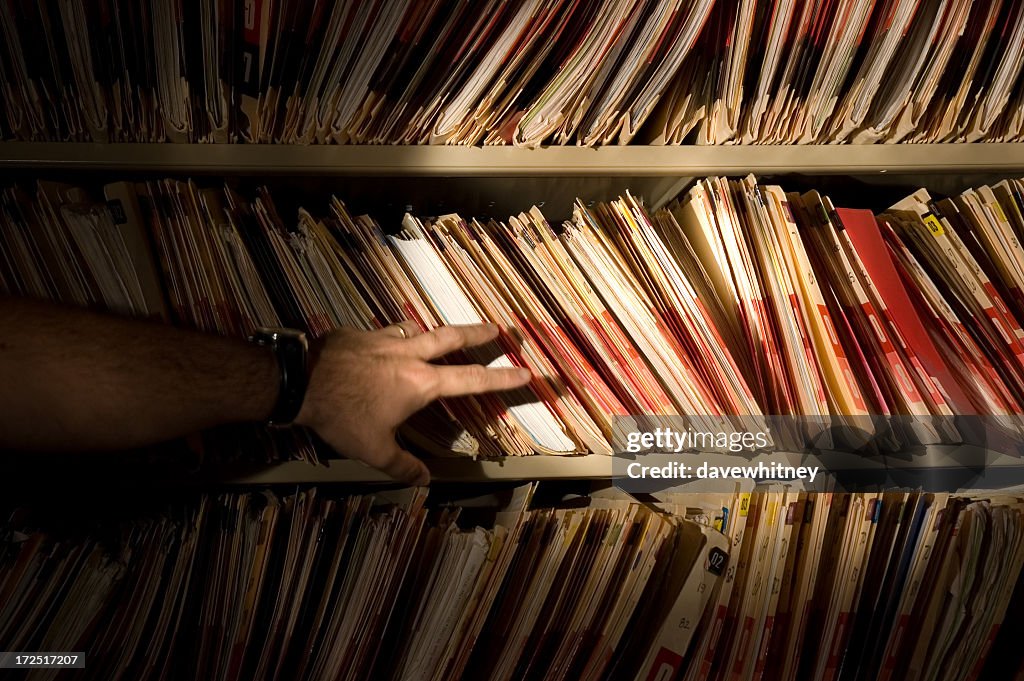 A man in front of a bookshelf of medical records