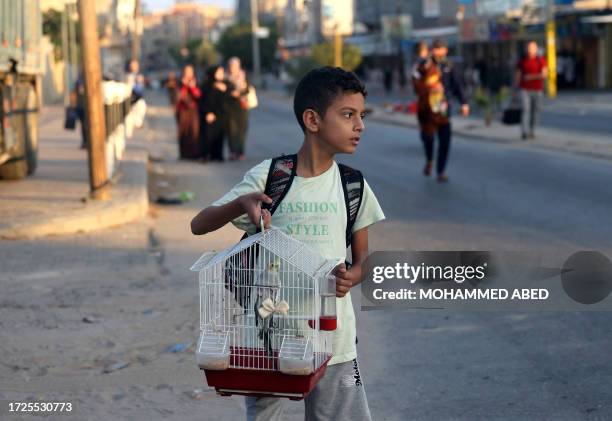 Palestinian boy carries his pet bird in a cage as families leave their homes following an Israeli attack on the Rafah refugee camp, in the southern...