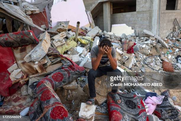 Palestinian youth reacts as he sits on the rubble of a destroyed home following an Israeli military strike on the Rafah refugee camp, in the southern...