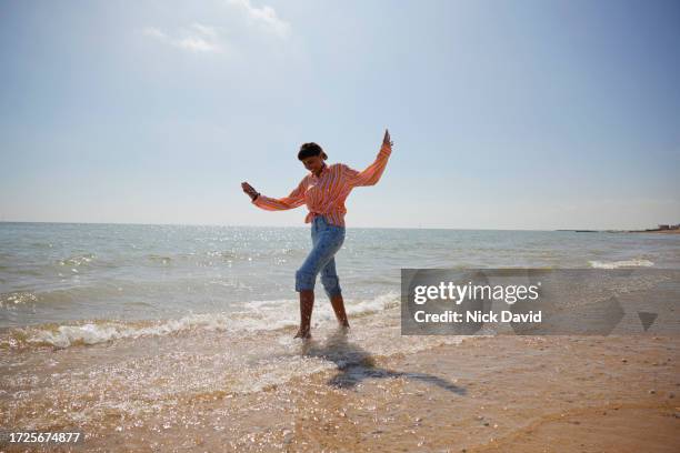 a young women enjoying a seaside paddle along an empty stretch of beach - skipping along stock pictures, royalty-free photos & images