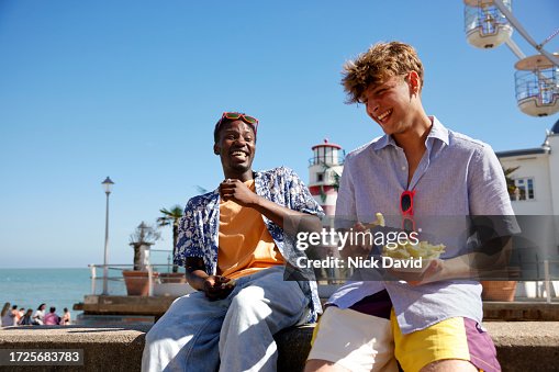 Two young male adults sharing food together at the seaside Two young male adults sharing food together at the seaside
