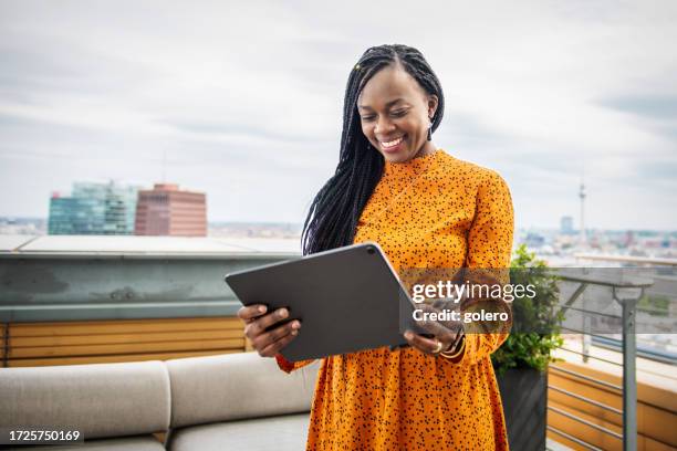 lächelnde schwarze geschäftsfrau schaut auf digitales tablet auf dachterrasse in berlin - berlin diversity alexanderplatz stock-fotos und bilder