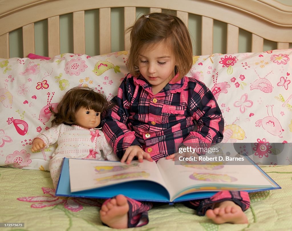 Small girl reading to her doll in bed