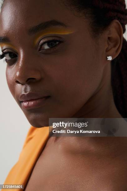 close up beauty portrait of afro american young woman with earring and yellow make-up and dress. beauty concept with copy space. - ear close up women stock-fotos und bilder