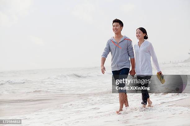 young couple walking by the waters edge on the beach, china - young couple beach stock pictures, royalty-free photos & images