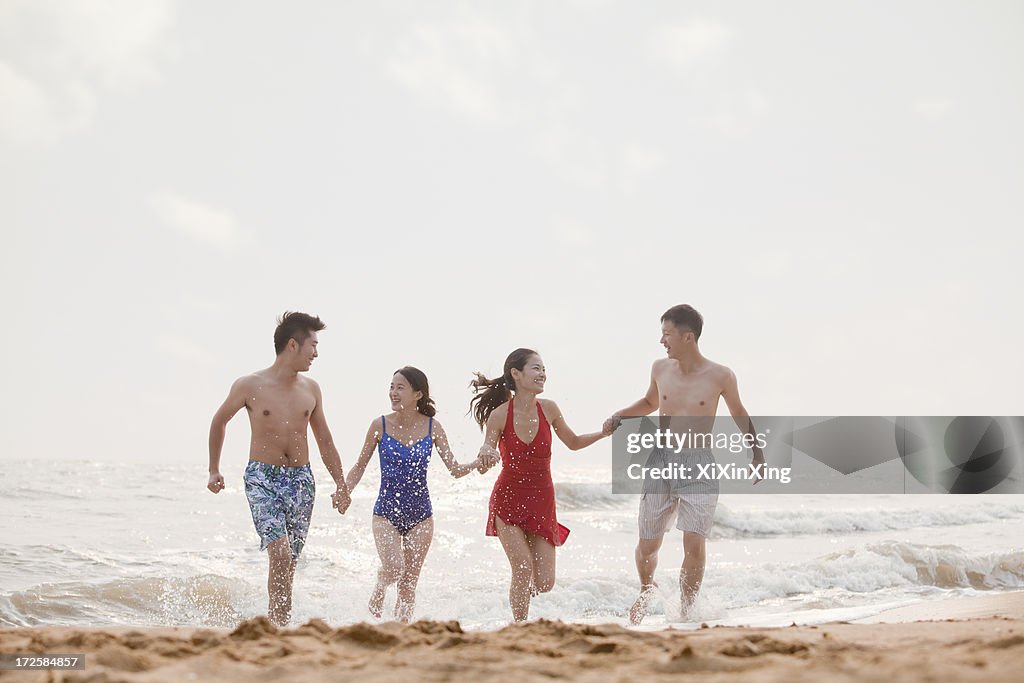 Four friends running out of the water on a sandy beach