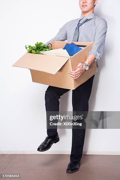 young businessman holding box of office items - rauswerfen stock-fotos und bilder