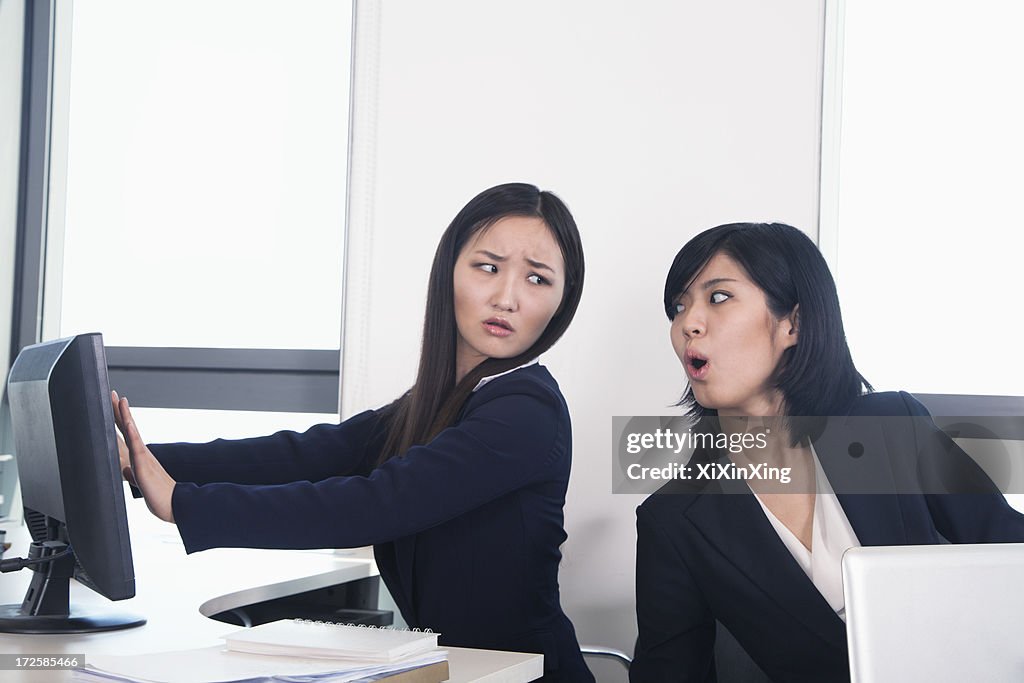 Officer worker hiding her computer from coworker