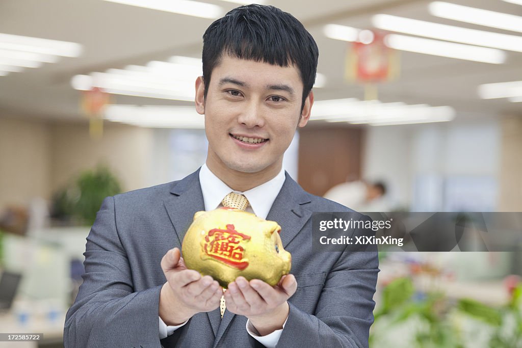 Young business man holding Chinese piggy bank, portrait