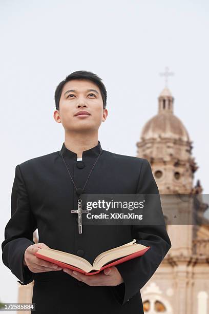 young priest looking to sky in front of church - priest collar stock pictures, royalty-free photos & images