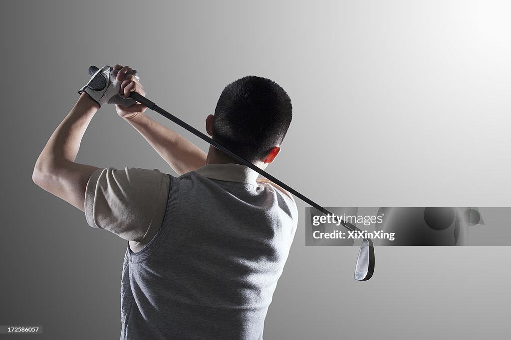 Young golf player swinging, rear view