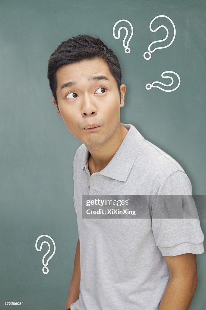 Portrait young man in front of blackboard with question marks