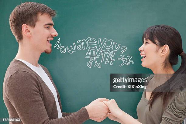 portrait of smiling male teacher and student in front of chalkboard holding hands - langues étrangères photos et images de collection