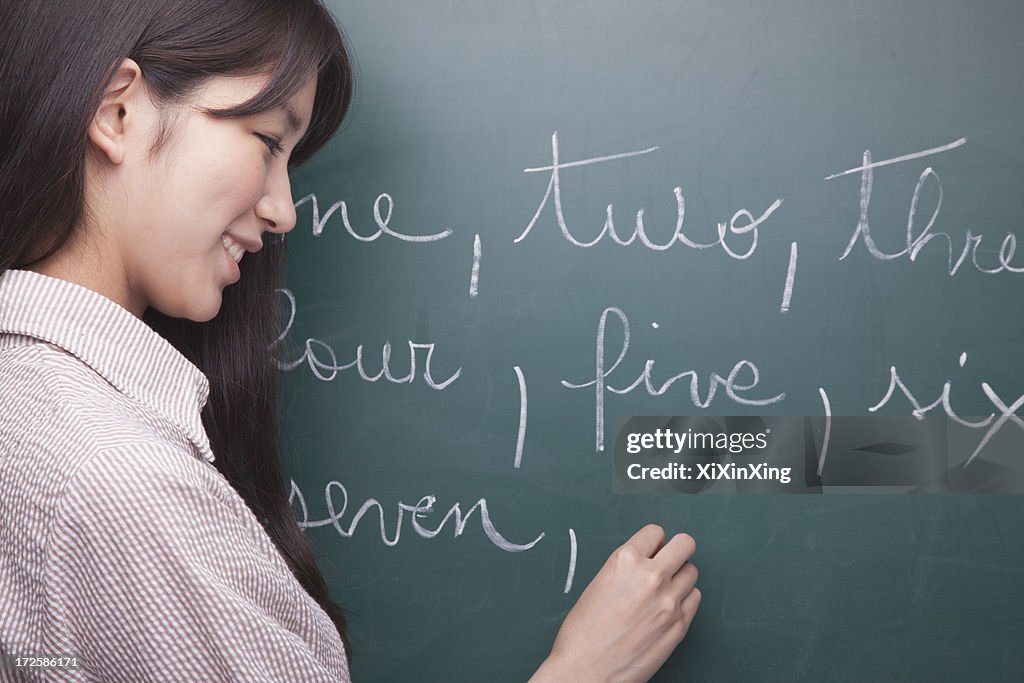 Young woman student writing English numbers on blackboard