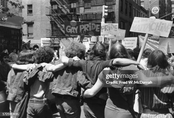 People hold 'Gay Pride' and 'Mattachine' signs during the first Stonewall anniversary march, then known as Gay Liberation Day , as they parade arm in...