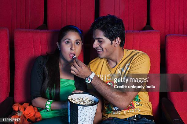man feeding popcorn to his girlfriend during watching movie in a cinema hall - indian couple in theaters stock pictures, royalty-free photos & images