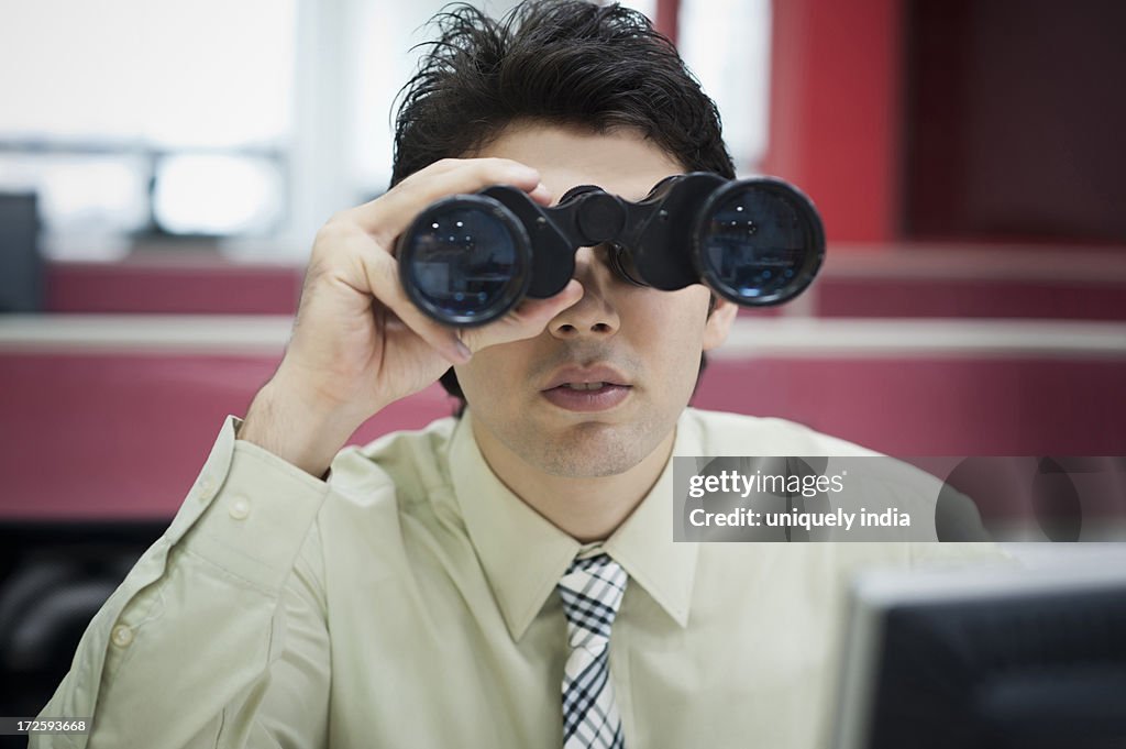 Businessman looking through binoculars in office