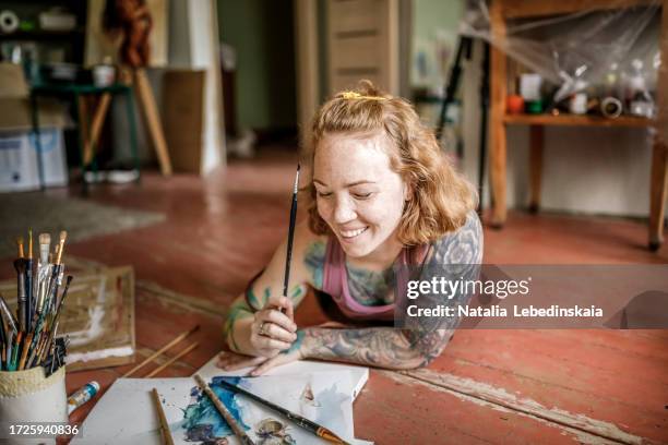 watercolor artistry: middle-aged woman with tattoos expresses creativity with a smile on the studio floor - hand smile painted stock-fotos und bilder