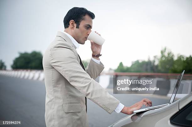 businessman drinking soft drink while using a laptop on car bonnet at the flyover - drinking soda in car stock pictures, royalty-free photos & images