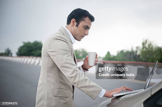 businessman holding soft drink while using a laptop on car bonnet at the flyover - drinking soda in car stock pictures, royalty-free photos & images