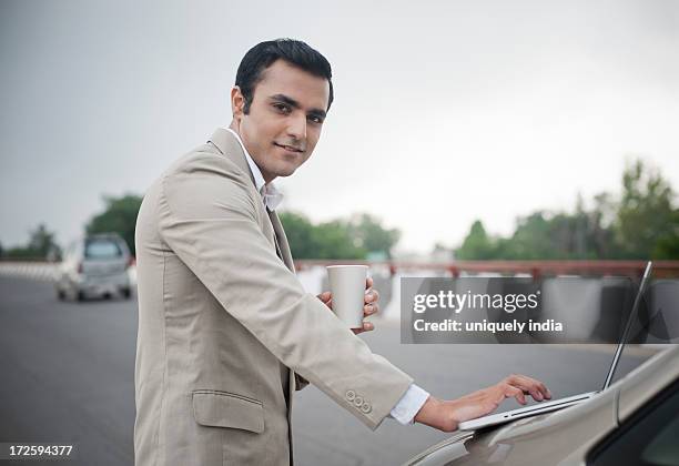 businessman holding soft drink while using a laptop on car bonnet at the flyover - drinking soda in car stock pictures, royalty-free photos & images