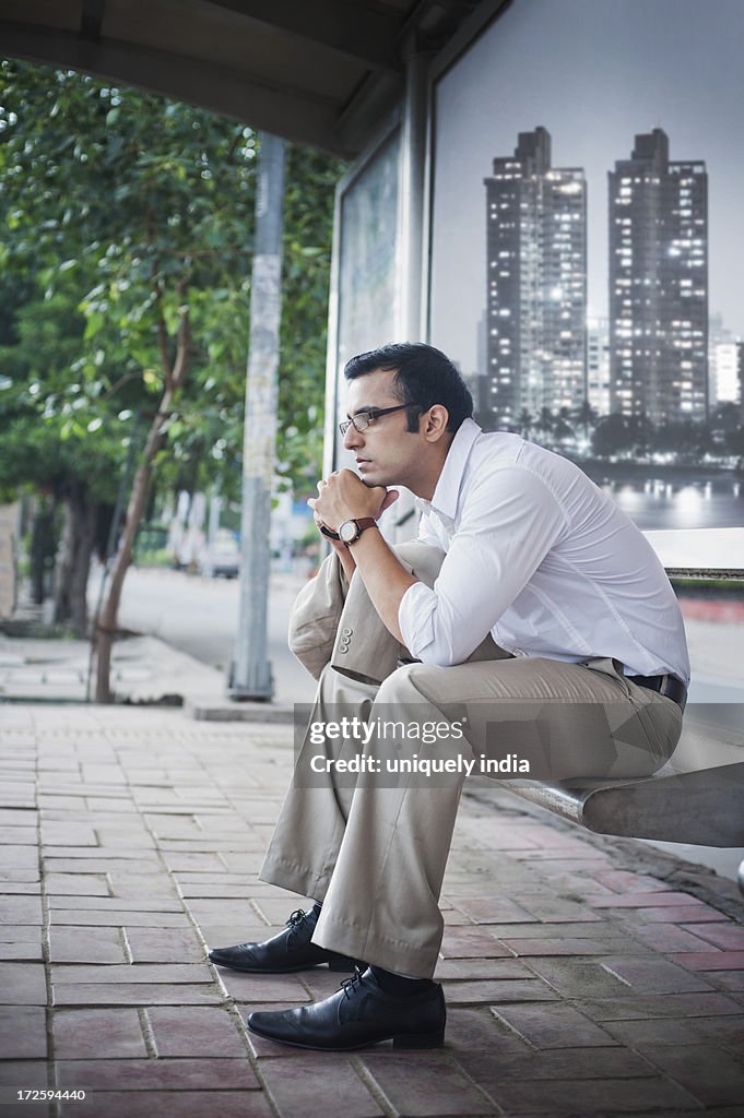 Businessman sitting on a bench at bus stop and looking thoughtful