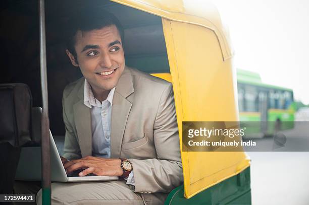 businessman using laptop and smiling while traveling in an auto rickshaw - jinrikisha stock pictures, royalty-free photos & images