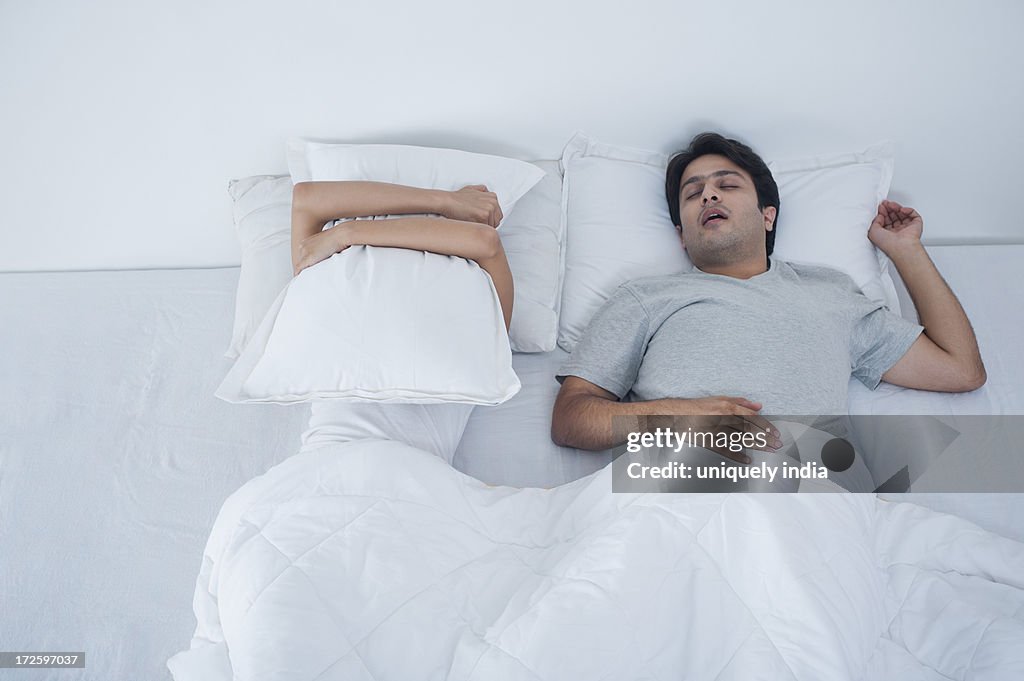 Man snoring with his wife covering her face with pillow on bed