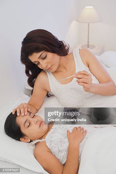 mother looking at a thermometer and touching the forehead of her daughter - bedside table kid asleep stock pictures, royalty-free photos & images