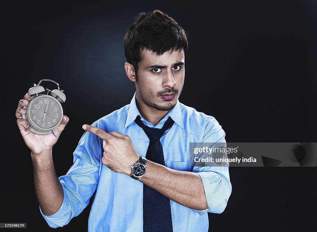 Angry businessman pointing towards an alarm clock