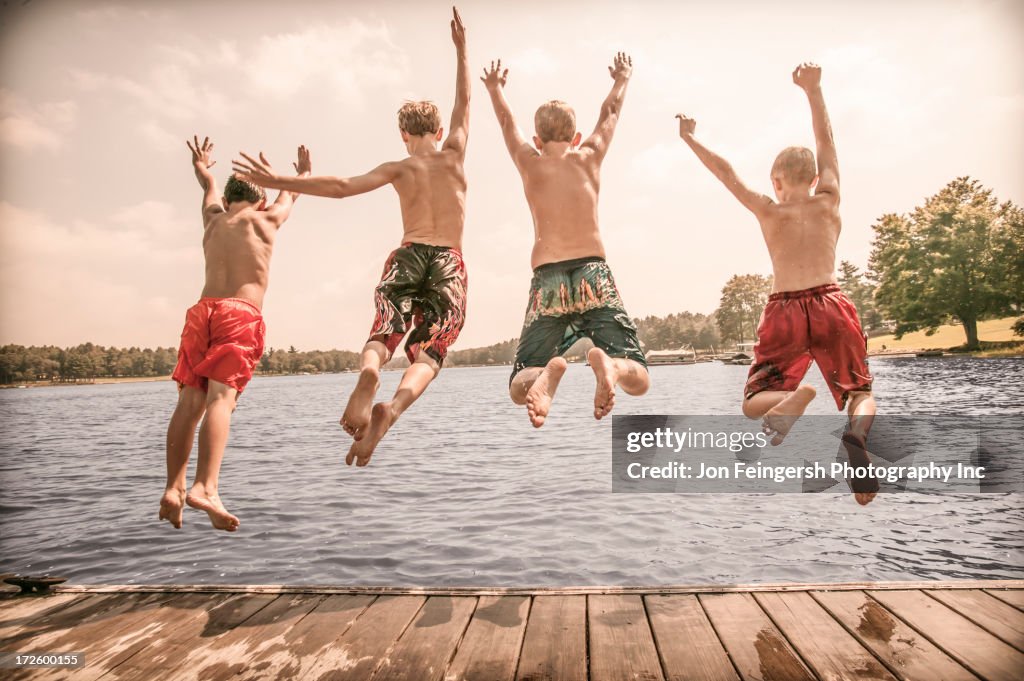 Caucasian boys jumping off wooden dock
