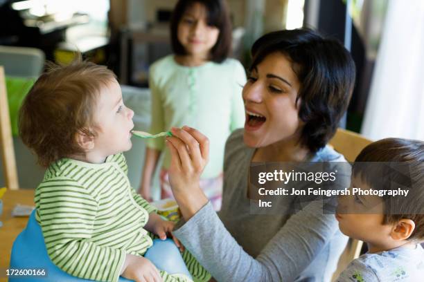 hispanic mother feeding toddler in kitchen - germantown maryland stock pictures, royalty-free photos & images