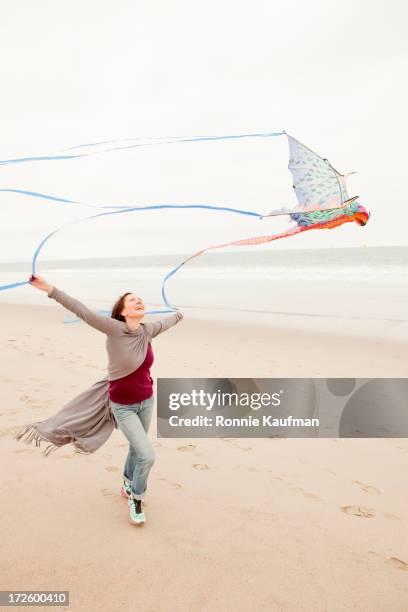 older caucasian woman flying kite on beach - kite toy stock pictures, royalty-free photos & images