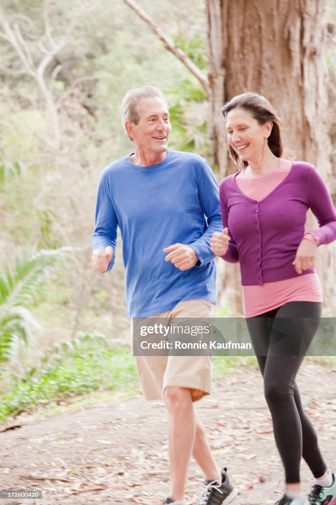 Older Caucasian couple jogging in forest