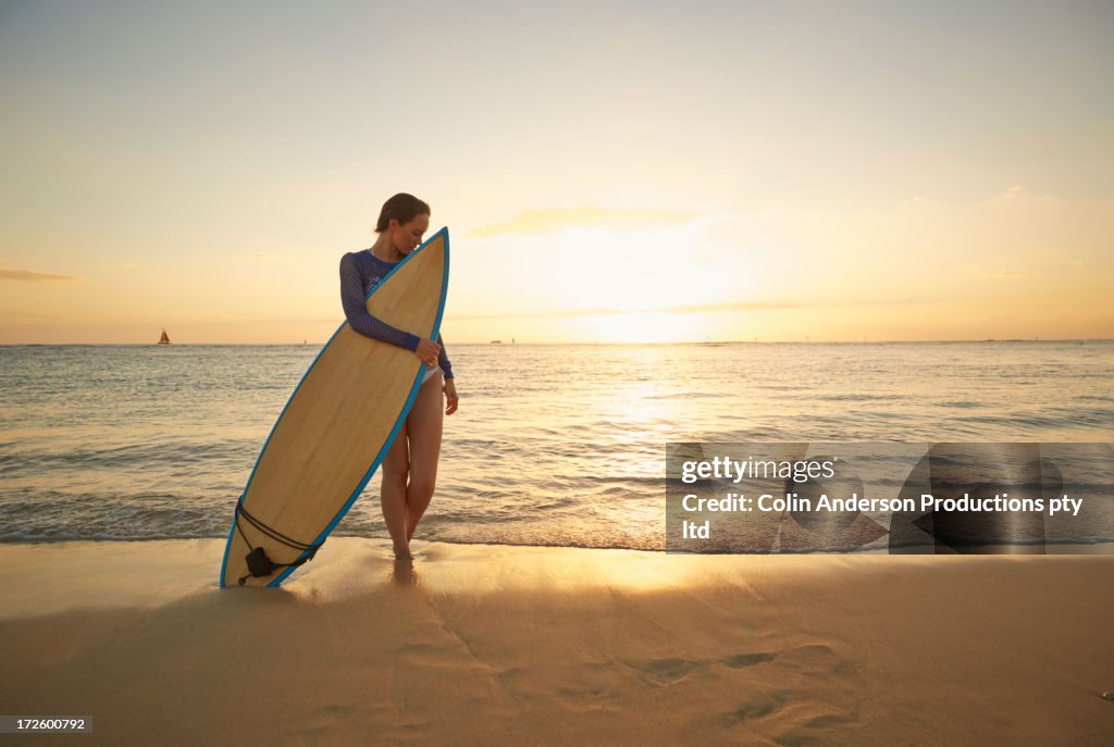 Pacific Islander woman holding surfboard on beach