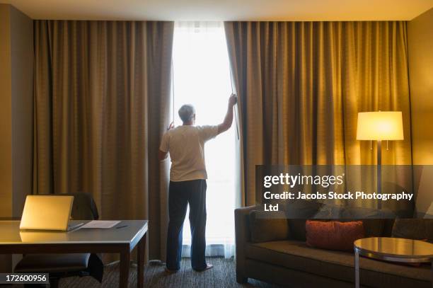 older caucasian man opening hotel curtains - curtain hotel stock-fotos und bilder