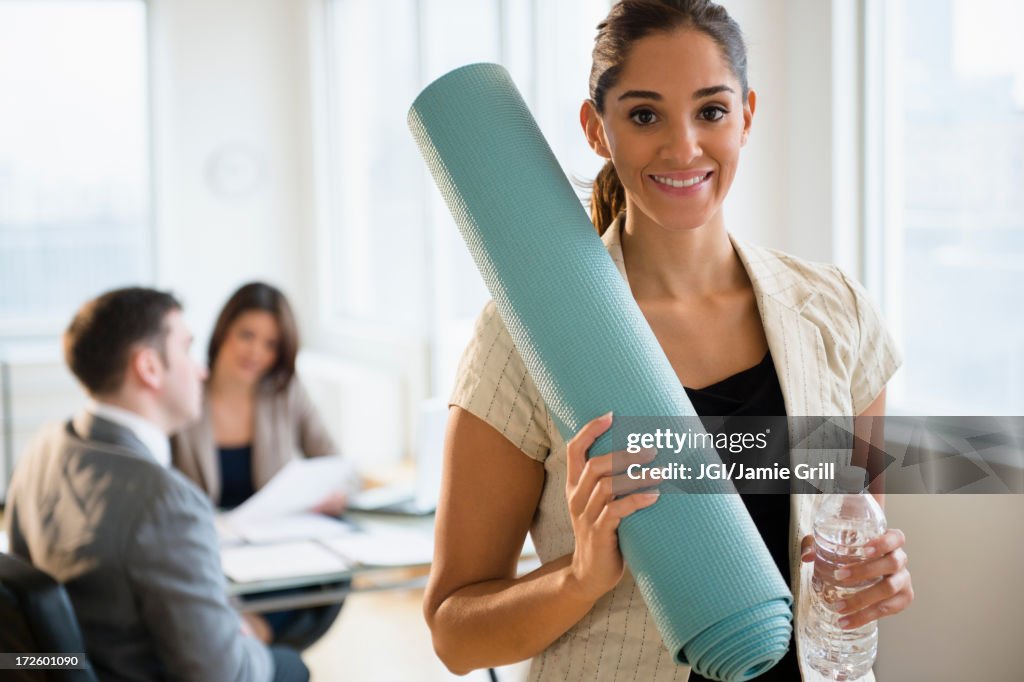 Businesswoman holding yoga mat in office