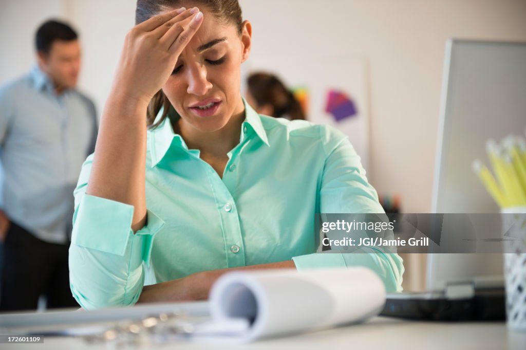 Businesswoman rubbing her forehead at desk