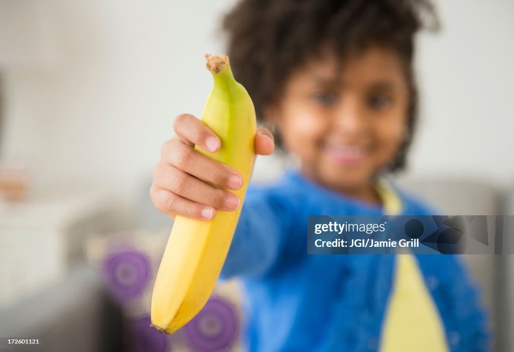 African American girl holding banana on sofa