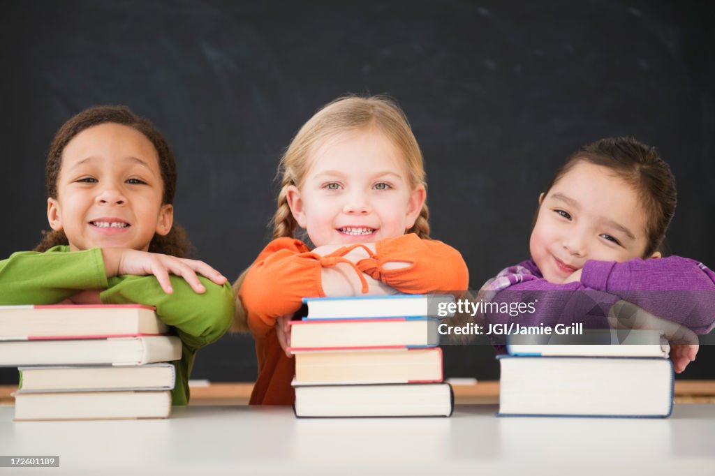 Girls leaning on stacks of books in classroom