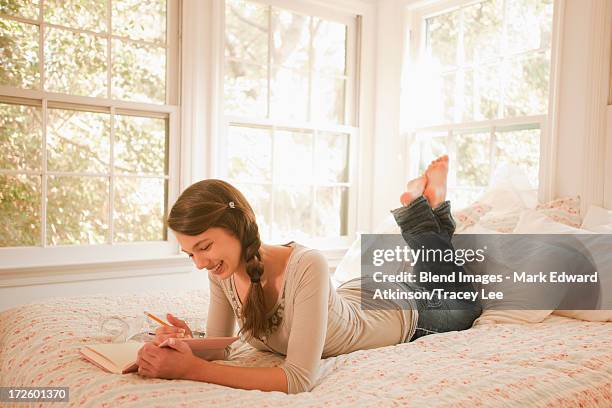 mixed race girl laying in bed writing in journal - teen girl barefoot at home stock pictures, royalty-free photos & images