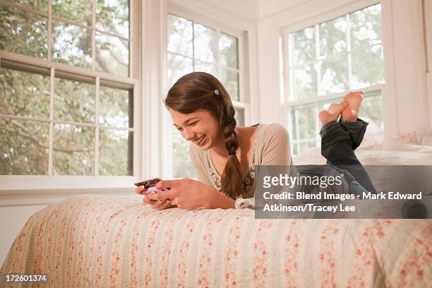 mixed race girl laying in bed text messaging on cell phone - teen girl barefoot at home stock pictures, royalty-free photos & images