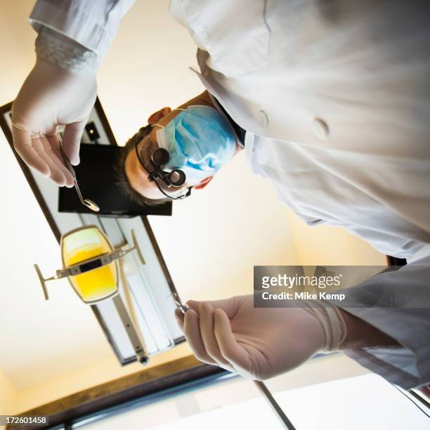 caucasian dentist towering over patient in office - surgical loupes stock pictures, royalty-free photos & images